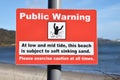 Red rectangular public warning sign with blurred beach background. Warning of soft sinking sand a low and mid tide. Royalty Free Stock Photo