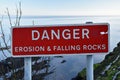 Red and white sign Danger Erosion and Falling Rocks with blurred background of sea and rocks Royalty Free Stock Photo