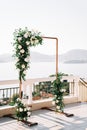 Rectangular wedding arch stands on a terrace above the sea against the backdrop of mountains