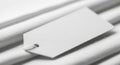 Rectangular white tag with a hole at one end, attached to a white textured surface using a string. Royalty Free Stock Photo