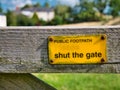 A rectangular, yellow, metal sign screwed to a wooden gate across a public footpath Royalty Free Stock Photo