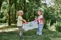 Recycling concept. Two cute little boy and girl holding recycle bin with plastic waste while standing in the forest or Royalty Free Stock Photo