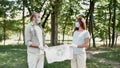 Two volunteers wearing protective face masks and gloves holding recycle bin with plastic waste and looking at each other