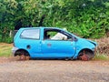 Abandoned blue junkyard car among the tropical vegetation of the French West Indies. Car scrap. Leftover of burnt out car at Royalty Free Stock Photo