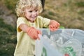 Recycling and Kids. Cute little boy wearing rubber gloves holding recycle bin and smiling while collecting plastic waste