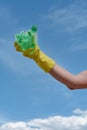 Recycling. Vertical shot of a volunteer wearing yellow rubbish glove holding used plastic bottle against blue sky