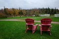 Red Adirondack Chairs on Green Lawn With Forest and Fall Foliage in Background Royalty Free Stock Photo