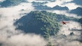 Red airplane flying over mountains with pine trees in the clouds. Royalty Free Stock Photo