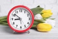 Red alarm clock and beautiful tulips on white wooden table against brick wall, closeup. Spring time Royalty Free Stock Photo