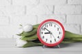 Red alarm clock and beautiful tulips on white wooden table against brick wall. Spring time Royalty Free Stock Photo