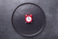 Red alarm clock and empty black ceramic plate on dark stone background. Intermittent fasting concept Royalty Free Stock Photo
