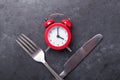 Red alarm clock, fork, knife and empty black ceramic plate on dark stone background. Intermittent fasting concept Royalty Free Stock Photo