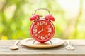 Red alarm clock, Fork, and spoon on wooden table with green outdoor nature blur background. Eight o'clock, Time for eating concep Royalty Free Stock Photo