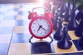 Red alarm clock near the black chessmen Royalty Free Stock Photo