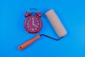 Red alarm clock and paint roller on blue background suggest themes of time, renovation, and creative transformation Royalty Free Stock Photo
