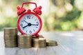 A red alarm clock and a pile of coins resting on the table. Ideas to save money, ideas for business growth, use the right time to