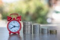 A red alarm clock and a pile of coins resting on the table. Ideas to save money, ideas for business growth, use the right time to