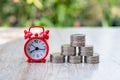 A red alarm clock and a pile of coins resting on the table. Ideas to save money, ideas for business growth, use the right time to