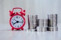 A red alarm clock and a pile of coins resting on the table. Ideas to save money, ideas for business growth, use the right time to