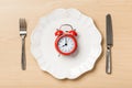 Red alarm clock on a plate, fork an knife on a table