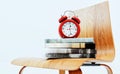 A red alarm clock sits on a pile of books on a wooden chair