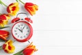 Red alarm clock, spring flowers and space for text on wooden table, flat lay. Time change