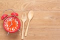 Red alarm clock in wooden dish, spoon and fork on wooden plank b Royalty Free Stock Photo