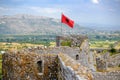 Red Albanian flag with double-headed black eagle waving over wall of Fortress Rozafa near Shkodra city. Fluttering banner with