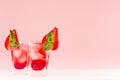 Red alcoholic shots of sweet fruit liquor with ice cubes, strawberry slice, green mint on pastel soft light pink background. Royalty Free Stock Photo
