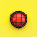 Red alert bulkhead light fixed to a painted yellow orange colour wall background. Photo in square format Royalty Free Stock Photo