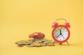 Red analog alarm clock ,blurred miniature car on pile of coins on yellow background, business and finance background Royalty Free Stock Photo