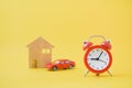 Red analog clock clock with blurred paper house and miniature car on yellow background, planning in future concept Royalty Free Stock Photo