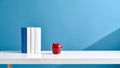 Red apple and books on a white table against a blue background. Royalty Free Stock Photo
