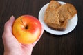 Red apple and bread pieces in plate on wooden background. Apple vs croissants, healthy food vs unhealthy food