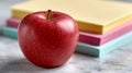 Red apple with colorful paper stack on marble surface. Royalty Free Stock Photo
