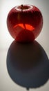 A red apple, covered in water droplets, sits on a smooth surface casting a long, oval Royalty Free Stock Photo