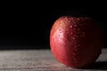 Red apple covered in water drops on black background with wooden floor. Health Concept with refreshing fruit
