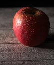 Red apple covered in water drops on black background with wooden floor. Health Concept with refreshing fruit