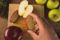 Red apple cut into slices on a kitchen board and a knife, surrounded by green apples. A man`s hand taking a piece of fruit Royalty Free Stock Photo