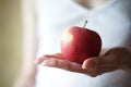 Red apple in female palm on the background of a girl in a white shirt Royalty Free Stock Photo