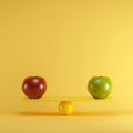 Red apple and green apple playing on yellow seesaw on blue background
