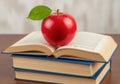 Red apple with green leaf resting on stack of open books Royalty Free Stock Photo