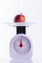 Red apple on kitchen weighing scales on white background