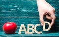 Red apple and letters of the ABCD. The hand puts the letter D to the others in a row. Apple for the teacher. Concept of education,