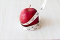 Red apple and measurement tape isolated on melamine wooden plank. Suitable for weight loss diet programme or advertisement.