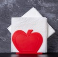 A red apple napkin holder with white napkins inserted into it. On a dark background.