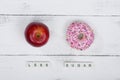 Red apple and a pink donut with tiles writing less sugar