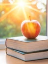A red apple sitting atop a stack of books in front of a window with bright sunlight shining through it Royalty Free Stock Photo