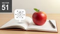 A red apple with a small green leaf rests on an open notebook on a wooden Royalty Free Stock Photo