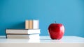 Red apple and stack of books on white surface against blue background. Royalty Free Stock Photo